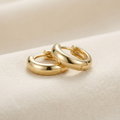 Gold huggie hoop earrings on cream background